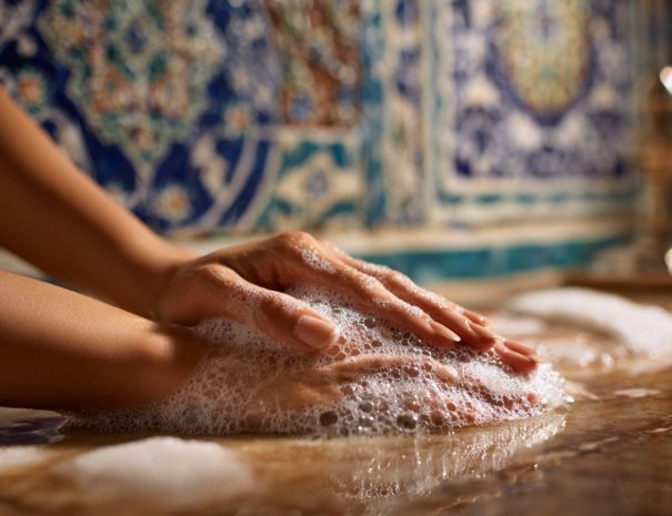 Nahaufnahme einer Hand, die in einem traditionellen Hammam mit duftendem Schaum gewaschen wird – orientalisches Reinigungsritual für Körper und Seele.