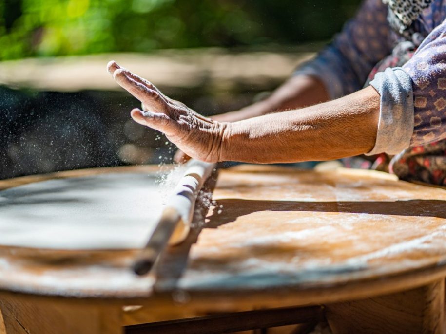 Mehlbestäubte Hände rollen traditionellen Teig auf Holzplatte – kulinarisches Handwerk im Freien bei der Lykia Lodge